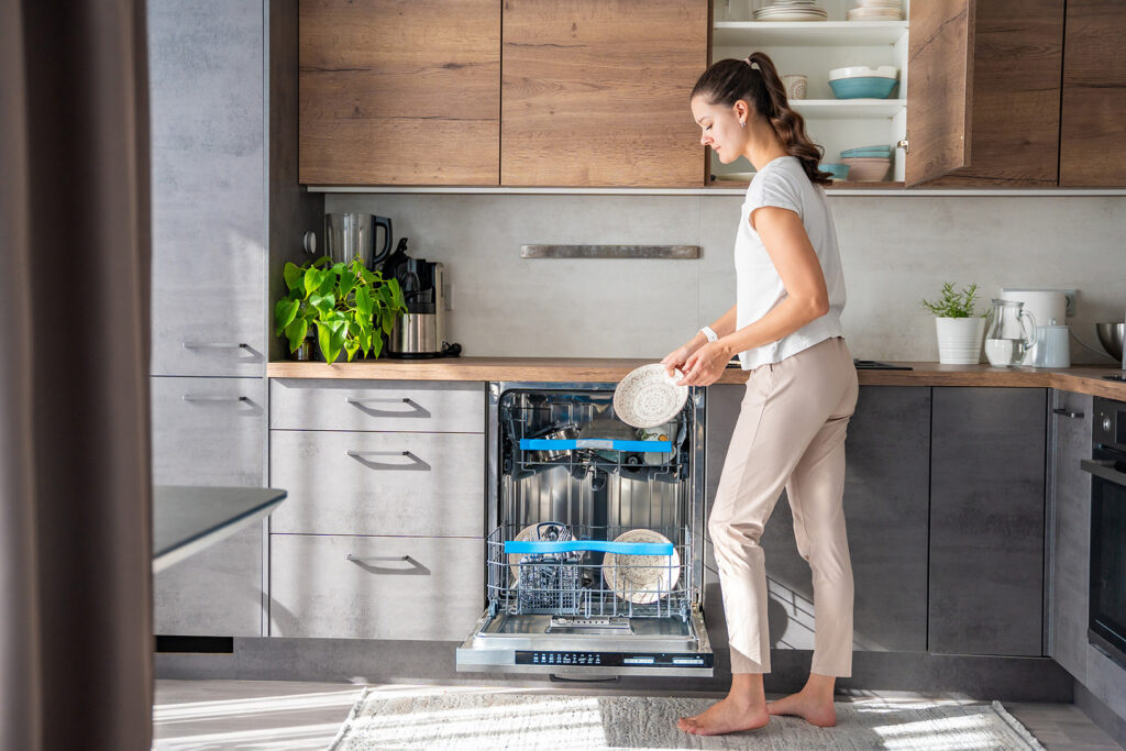 a woman removes clean ceramic dishes from the dishwasher. household and useful technology concept.
